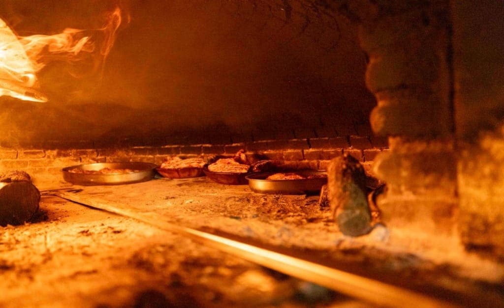 Llamas de leña dorando las cazuelas de lechazo en el horno